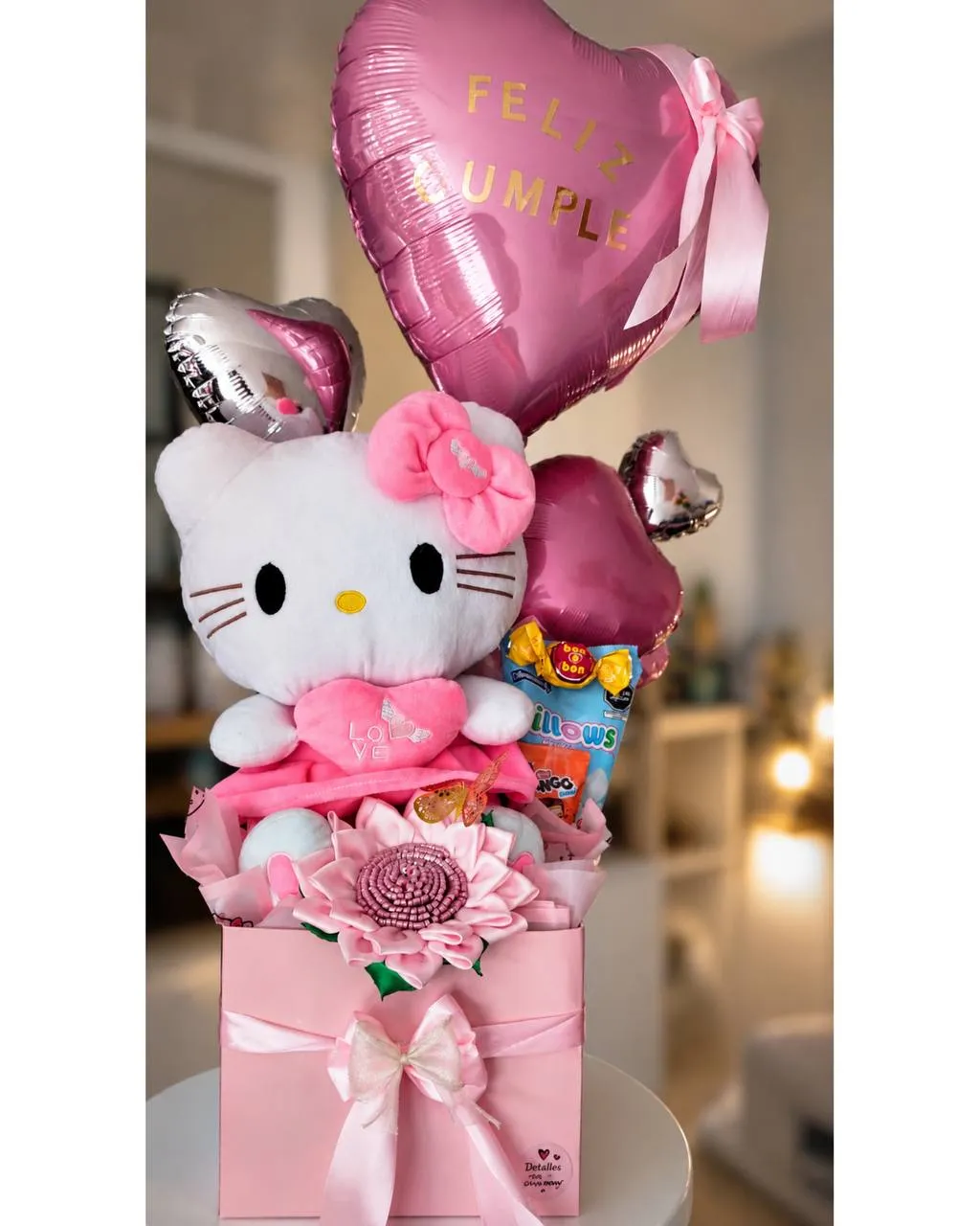 Arreglo sobre caja rosa con un peluche de gatita, globos de corazón, golosinas y una flor de tela.