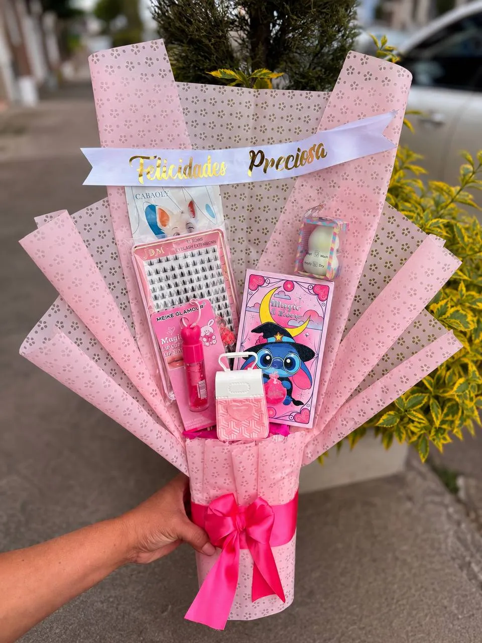 Ramo armado con productos de maquillaje, accesorios y una libreta ilustrada, con banda de felicitación.