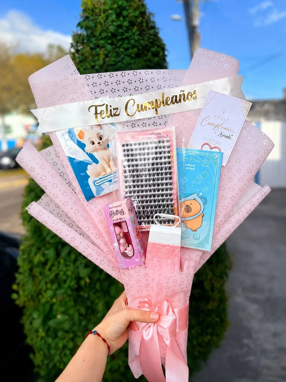 Ramo armado con productos de cuidado personal y una cinta de feliz cumpleaños, en envoltura rosa.