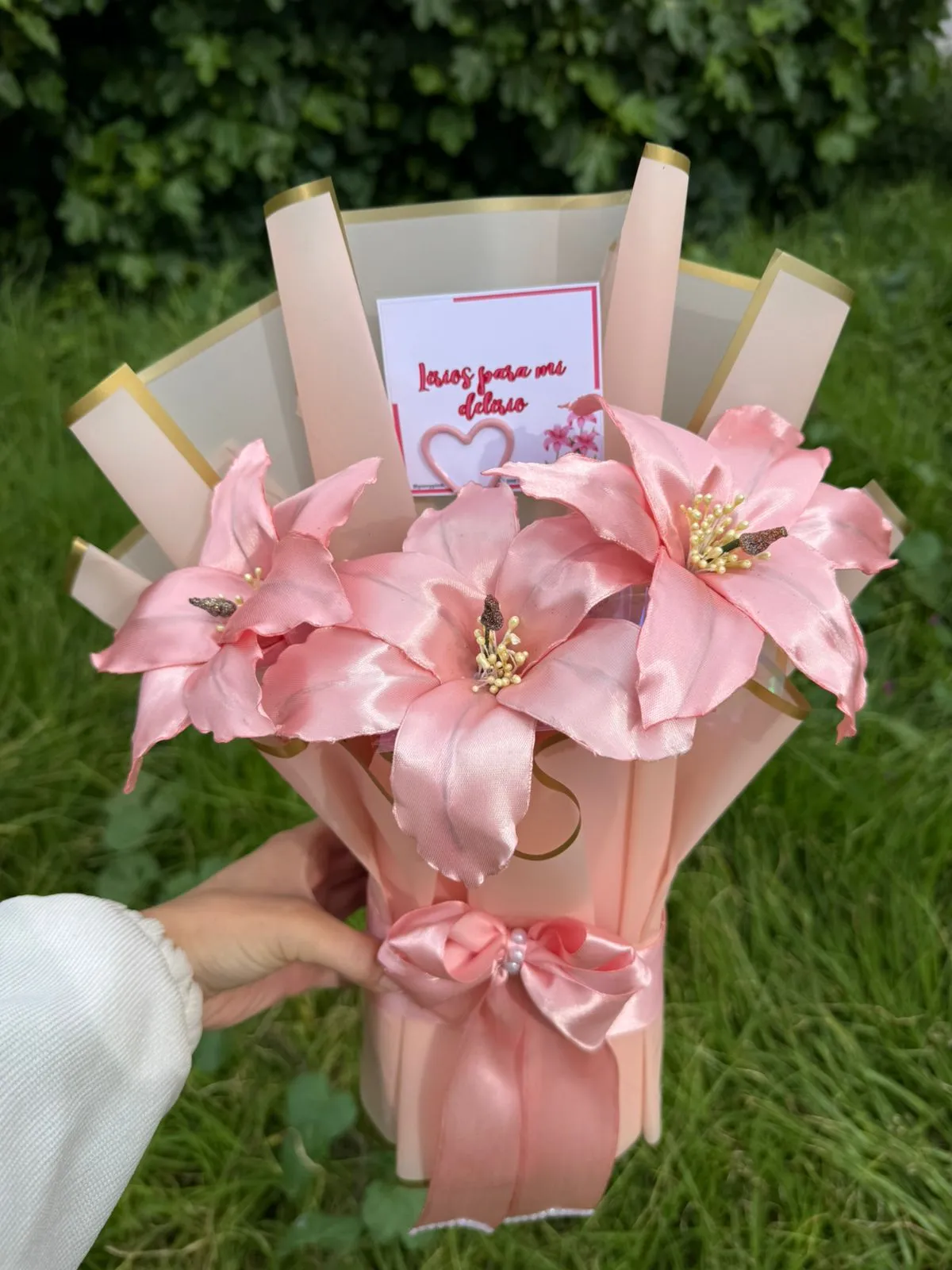 Ramo de lirios de cinta rosados con envoltura crema y rosa, lazo de raso y una tarjeta con una dedicatoria.
