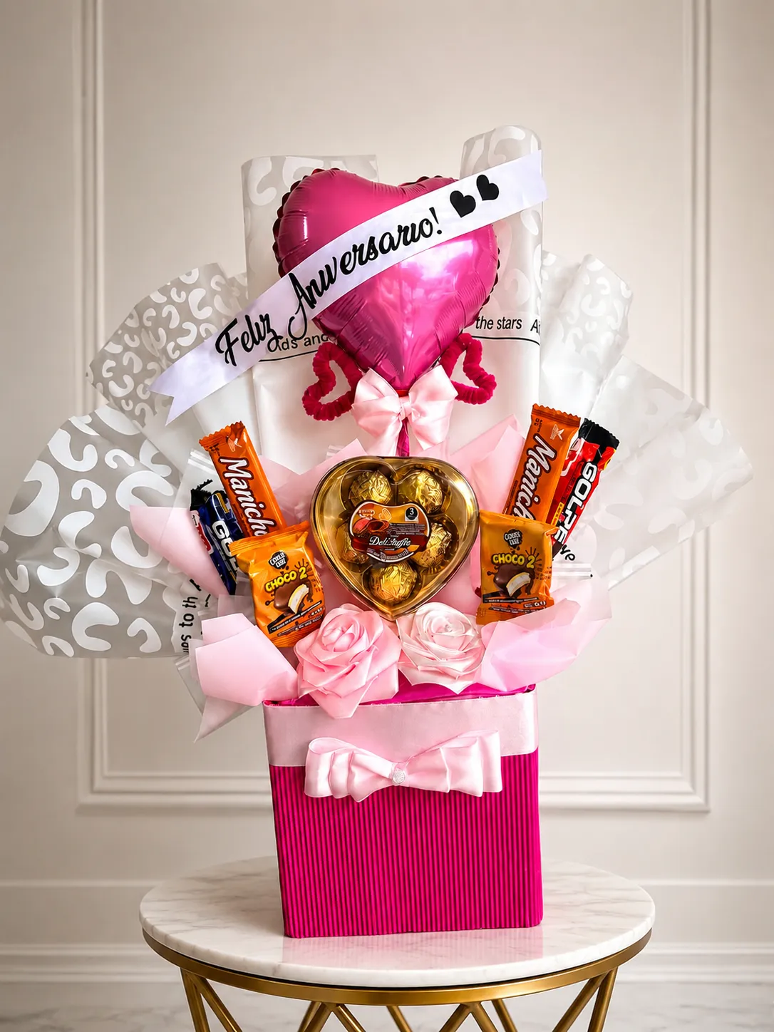 Caja fucsia con un globo de corazón de aniversario, bombones y golosinas entre rosas de cinta.