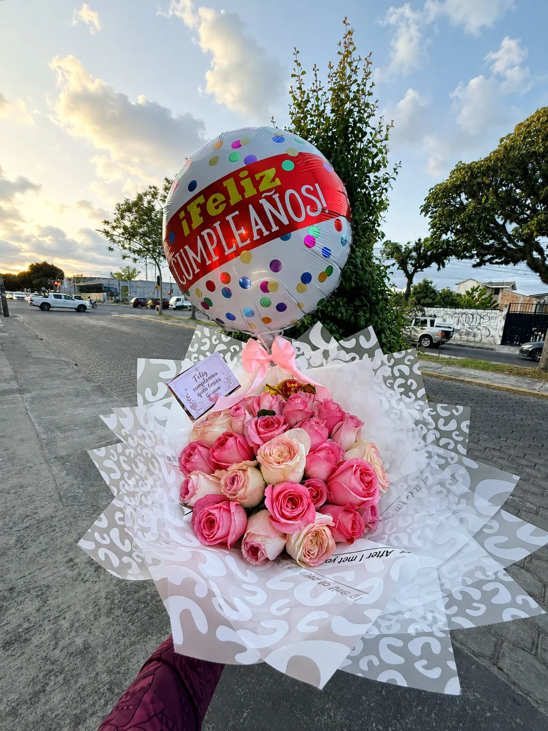 Ramo de rosas rosadas y crema con un globo redondo de feliz cumpleaños, al atardecer.