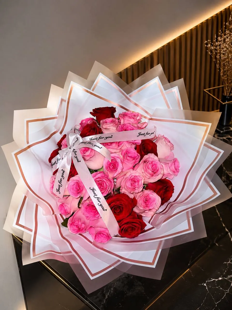 Ramo de rosas fucsia, rosadas y rojas con envoltura blanca de capas y borde dorado.