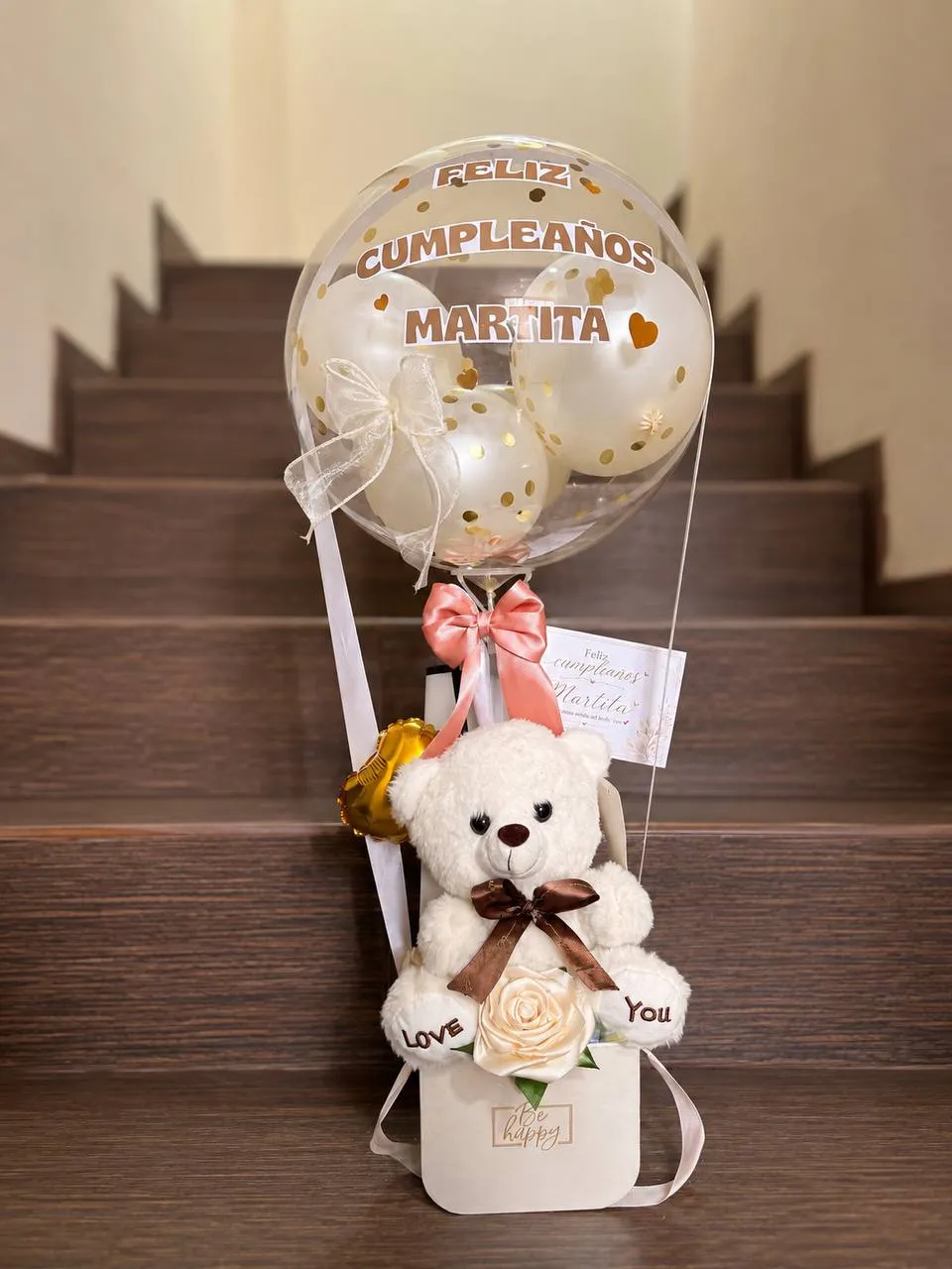 Arreglo con osito de peluche, una rosa de tela y un globo transparente personalizado con un nombre.