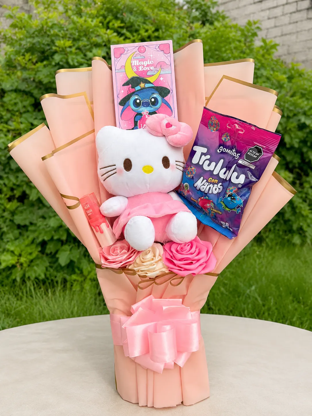 Ramo con un peluche de gatita, golosinas y rosas de cinta, en envoltura durazno con lazo rosa.