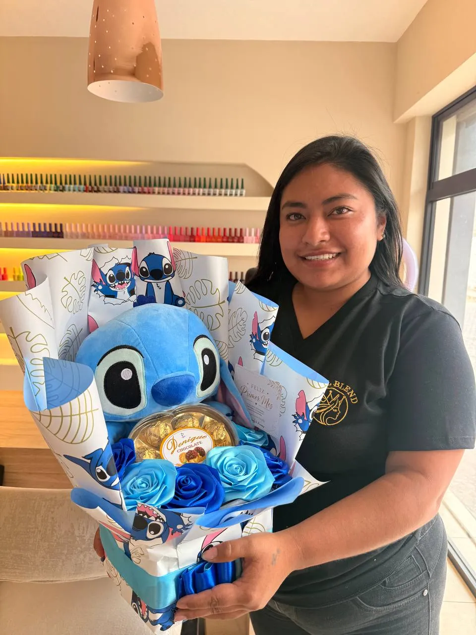 Una clienta sonríe sosteniendo un ramo con un peluche azul, rosas azules, chocolates y una tarjeta.
