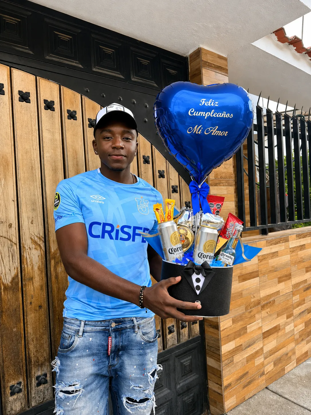 Un hombre sostiene una caja negra con bebidas, golosinas y un globo azul de corazón.